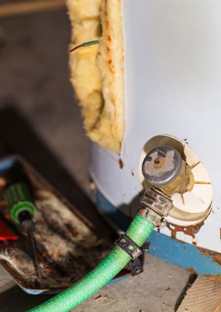 Descaling and flushing a water heater tank using a green drain hose and screwdriver